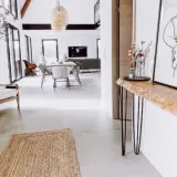 Una consolle fai da te con piano in legno grezzo e gambe sottili, decorata con un vaso di fiori secchi e un quadro astratto.