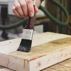 Mano che applica vernice su un pezzo di legno grezzo, un progetto fai da te in corso.
