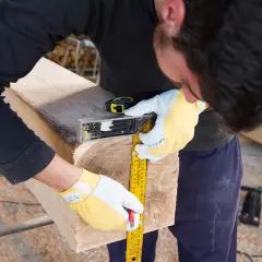 Uomo con guanti gialli misura un tronco per capire come tagliare il legno, usando un metro e una squadra.