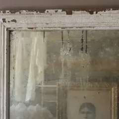 Cornice scrostata e specchio antico, con riflessi di un ritratto e tendaggi. Un modo per come invecchiare uno specchio, con patina del tempo.