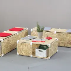 Set di mobili in OSB fai da te: tavolino e panche modulari con cuscini rossi e grigi, cestini portaoggetti e libri.