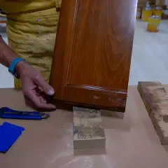 Un falegname esamina un pannello di legno con un piccolo buco, pronto per la riparazione.