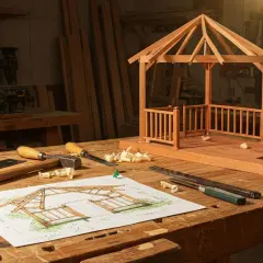 Un progetto di gazebo in legno fai da te, con schizzi, attrezzi e un modello in miniatura su un banco da falegname.