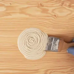 Mano con guanto blu applica stucco con pennello su legno. Guida pratica su come stuccare il legno per una finitura perfetta.