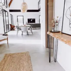 Una consolle fai da te con piano in legno grezzo e gambe sottili, decorata con un vaso di fiori secchi e un quadro astratto.