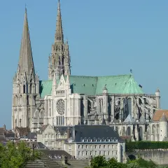 Imponente cattedrale gotica con guglie svettanti e tetto verde, che domina un paesaggio urbano sotto un cielo azzurro.
