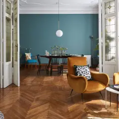 Soggiorno con poltrone ocra, tavolino moderno e un tavolo da pranzo in stile direttorio sullo sfondo. Porte a vetri decorati.