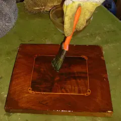 Guanto giallo applica liquido con pennello arancione su un mobile in legno scuro, per imparare come sverniciare un mobile.