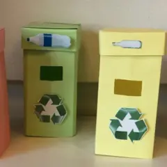 Quattro colorati contenitori per la raccolta differenziata fai da te, con simboli e immagini che indicano cosa gettare.