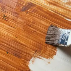 Pennello applica vernice marrone su legno, rinnovando una superficie già verniciata.