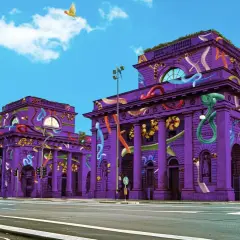 Edifici viola decorati con serpenti colorati e pappagalli volanti, un'installazione artistica che sembra un'opera fuori salone.