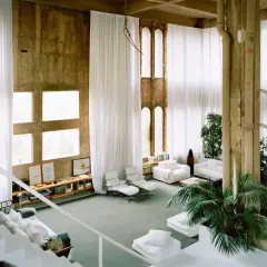 Interno spazioso con tende bianche, finestre quadrate e un'architettura industriale che ricorda lo stile di Ricardo Bofill.
