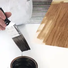 Pennello intinto in una latta, pronto per applicare un prodotto che mostra la differenza tra flatting e impregnante su legno.