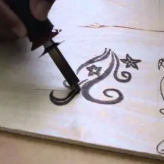 Mano che usa un pirografo per disegnare motivi floreali su legno. Impara come disegnare sul legno con questa tecnica.