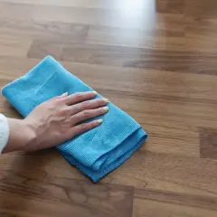 Mano con panno blu che pulisce il pavimento in legno, un metodo efficace per come togliere la colla dal legno.