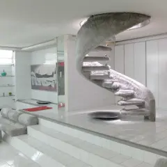 Interni futuristici con scala a chiocciola rivestita in pelliccia, un omaggio a Nanda Vigo. Divani e pouf morbidi completano l'ambiente.