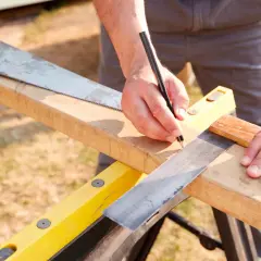 Mani che prendono le **misure per fare una squadra** perfetta su un pezzo di legno, con una sega e una matita a portata di mano.