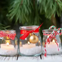 Candele in barattoli decorati con nastri rossi, fiocchi e palline dorate. Un'idea per addobbi natalizi fai da te, con un tocco di magia.