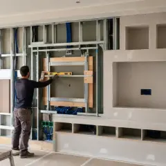 Costruzione di una parete attrezzata fai da te: un uomo usa una livella per montare la struttura metallica per un mobile TV.