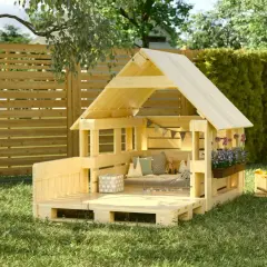 Una capanna per bambini fai da te in legno, con cuscini, fiori e giochi, pronta per l'avventura in giardino.