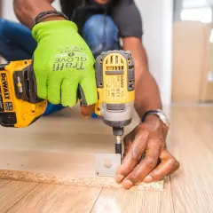 Uomo con guanti verdi usa un trapano per fresare il legno, creando fori precisi per un progetto fai-da-te.