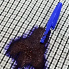 Una penna blu ha creato una grossa macchia d'inchiostro su una camicia a quadri.