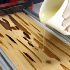 Mano guantata versa resina epossidica su legno con fessure, mostrando come usare la resina epossidica sul legno per creare un effetto lucido.