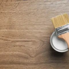 Pennello pronto per dipingere legno. La latta di vernice bianca è aperta, il legno è pronto per il restauro.