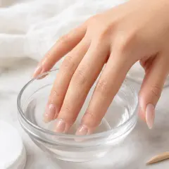 Mano con unghie immerse in una ciotola d'acqua, per rimuovere la colla per unghie dal tavolo.