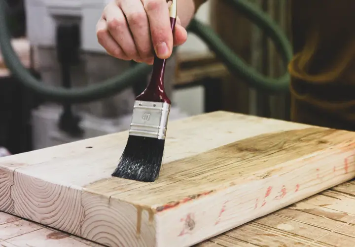 Mano che applica vernice su un pezzo di legno grezzo, un progetto fai da te in corso.