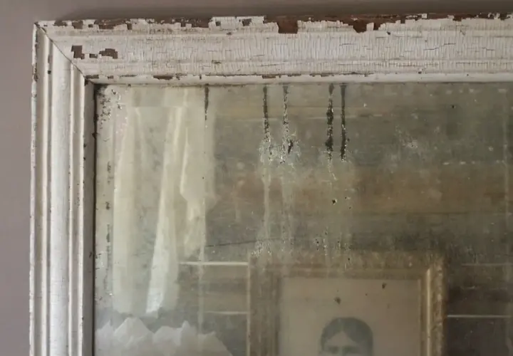 Cornice scrostata e specchio antico, con riflessi di un ritratto e tendaggi. Un modo per come invecchiare uno specchio, con patina del tempo.