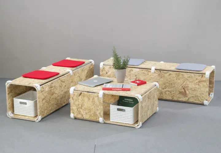 Set di mobili in OSB fai da te: tavolino e panche modulari con cuscini rossi e grigi, cestini portaoggetti e libri.