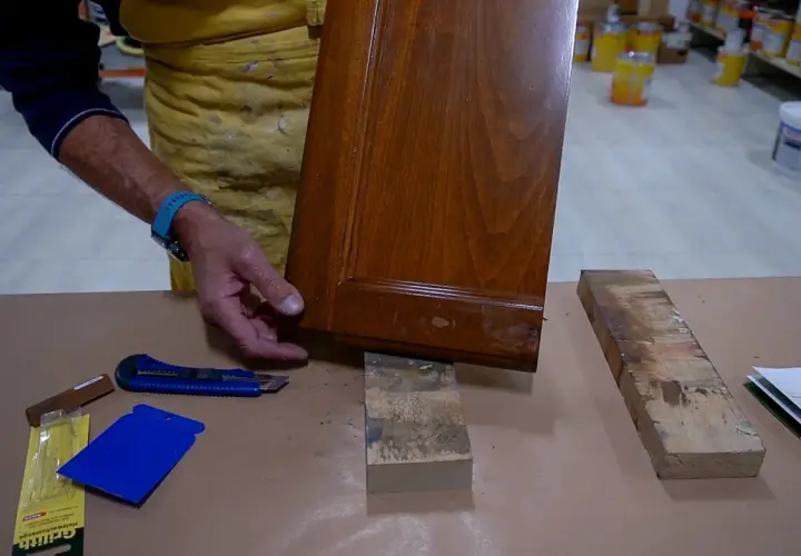 Un falegname esamina un pannello di legno con un piccolo buco, pronto per la riparazione.