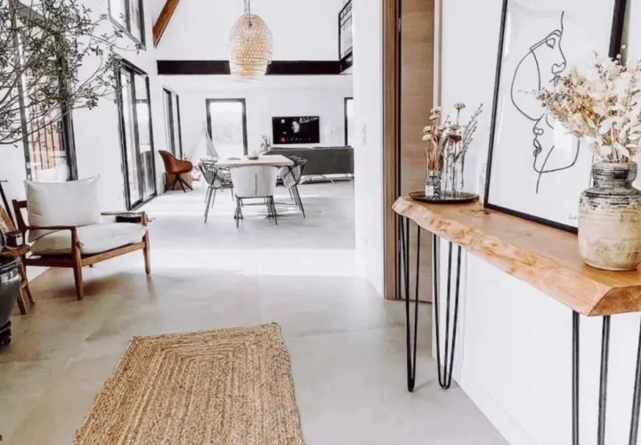 Una consolle fai da te con piano in legno grezzo e gambe sottili, decorata con un vaso di fiori secchi e un quadro astratto.