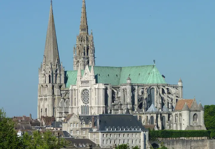 Imponente cattedrale gotica con guglie svettanti e tetto verde, che domina un paesaggio urbano sotto un cielo azzurro.