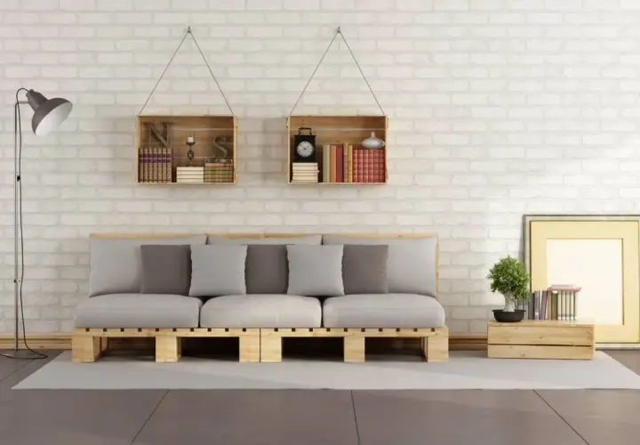 Divano pallet fai da te con cuscini grigi e bianchi, librerie a muro in legno e lampada da terra.