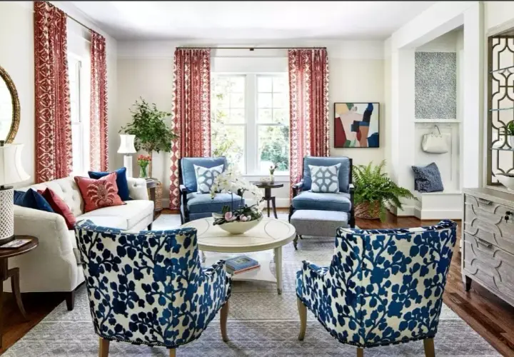 Salotto in stile grandmillennial con divano bianco, poltrone blu e sedie con fantasia floreale blu e bianca. Tende rosse e specchio dorato.