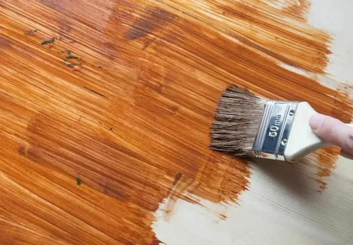 Pennello applica vernice marrone su legno, rinnovando una superficie già verniciata.