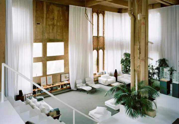 Interno spazioso con tende bianche, finestre quadrate e un'architettura industriale che ricorda lo stile di Ricardo Bofill.