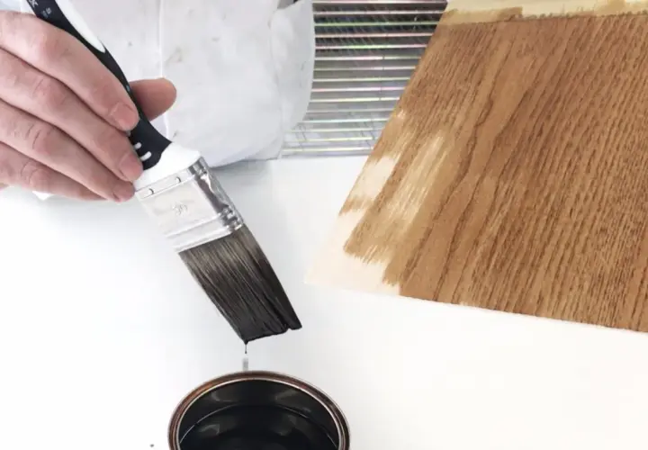 Pennello intinto in una latta, pronto per applicare un prodotto che mostra la differenza tra flatting e impregnante su legno.