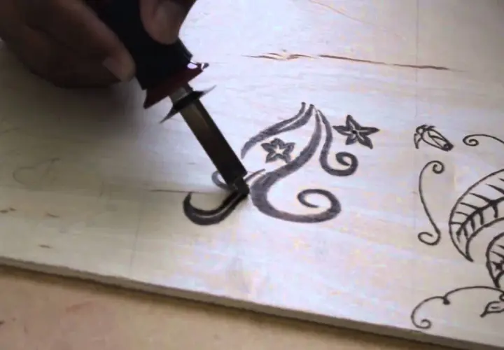 Mano che usa un pirografo per disegnare motivi floreali su legno. Impara come disegnare sul legno con questa tecnica.