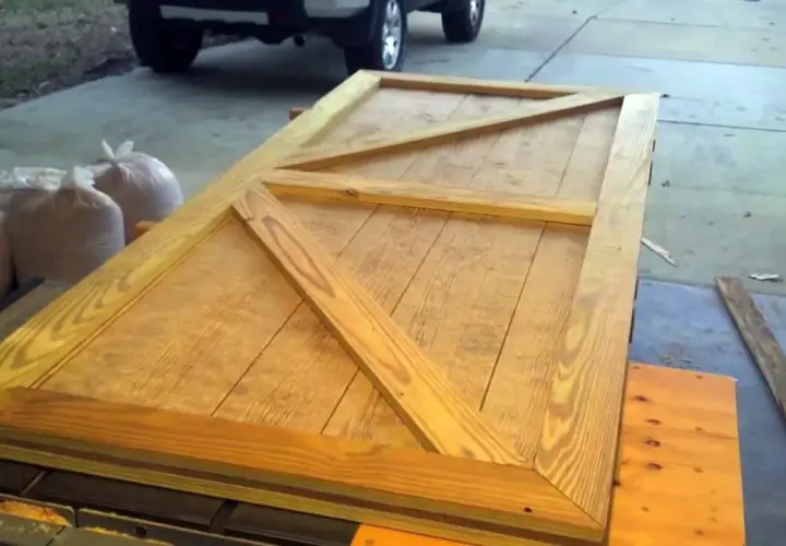 Porta fai da te per esterno in legno grezzo, con rinforzi a X, pronta per essere installata.