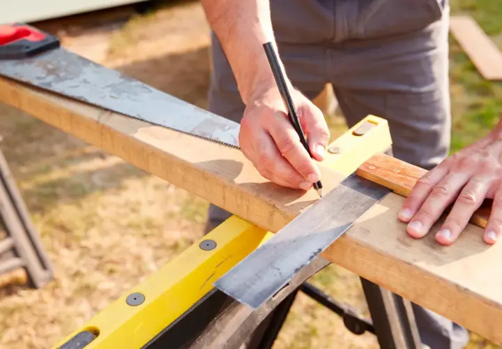 Mani che prendono le **misure per fare una squadra** perfetta su un pezzo di legno, con una sega e una matita a portata di mano.