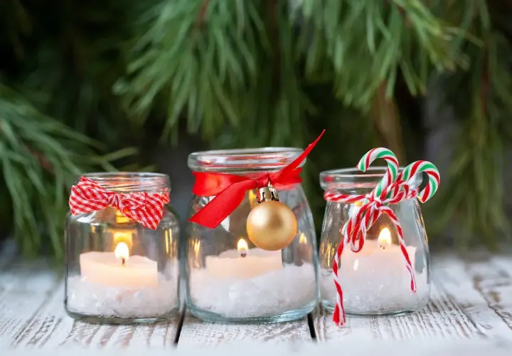 Candele in barattoli decorati con nastri rossi, fiocchi e palline dorate. Un'idea per addobbi natalizi fai da te, con un tocco di magia.