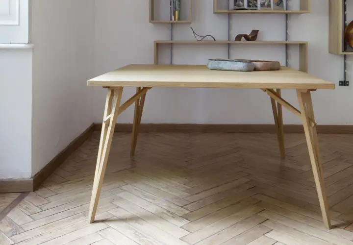 Tavolo pieghevole fai da te in legno chiaro, con gambe a incastro e piano squadrato. Due ciotole decorative sul piano.