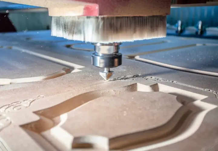La fresa CNC sta lavorando il legno, creando un intricato motivo decorativo. La polvere di legno vola mentre la macchina esegue il suo lavoro di precisione.