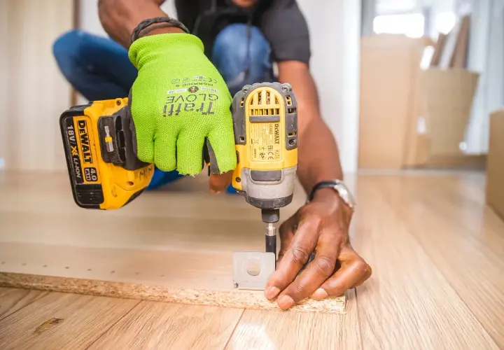 Uomo con guanti verdi usa un trapano per fresare il legno, creando fori precisi per un progetto fai-da-te.