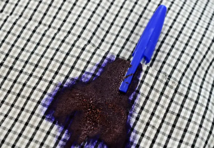 Una penna blu ha creato una grossa macchia d'inchiostro su una camicia a quadri.