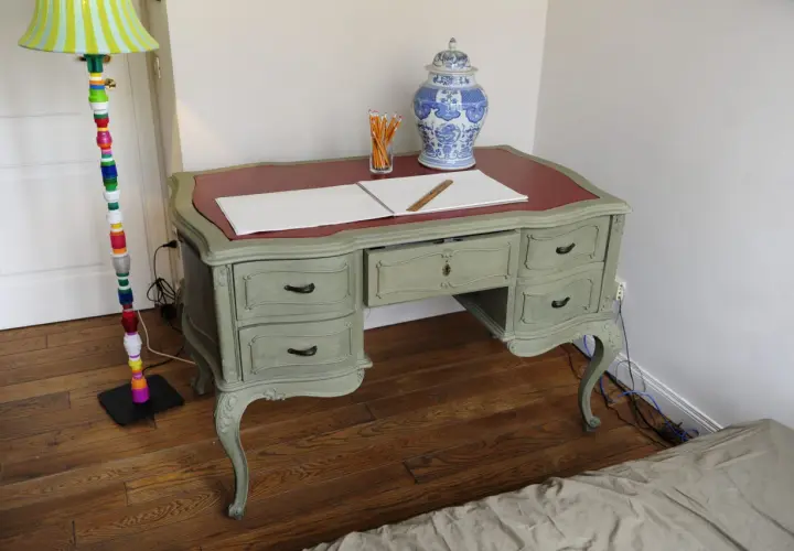 Scrivania in stile shabby chic, con finitura chalk paint fai da te. Penzoli, un righello e un vaso decorato completano la scena.