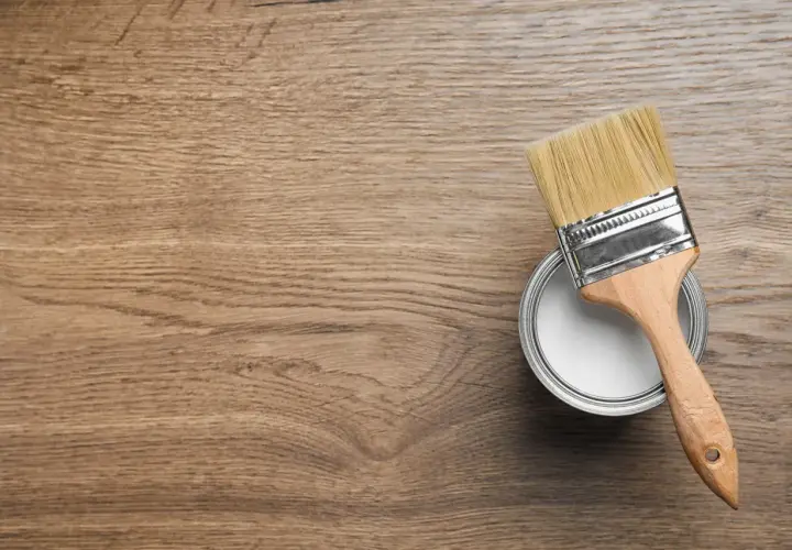 Pennello pronto per dipingere legno. La latta di vernice bianca è aperta, il legno è pronto per il restauro.